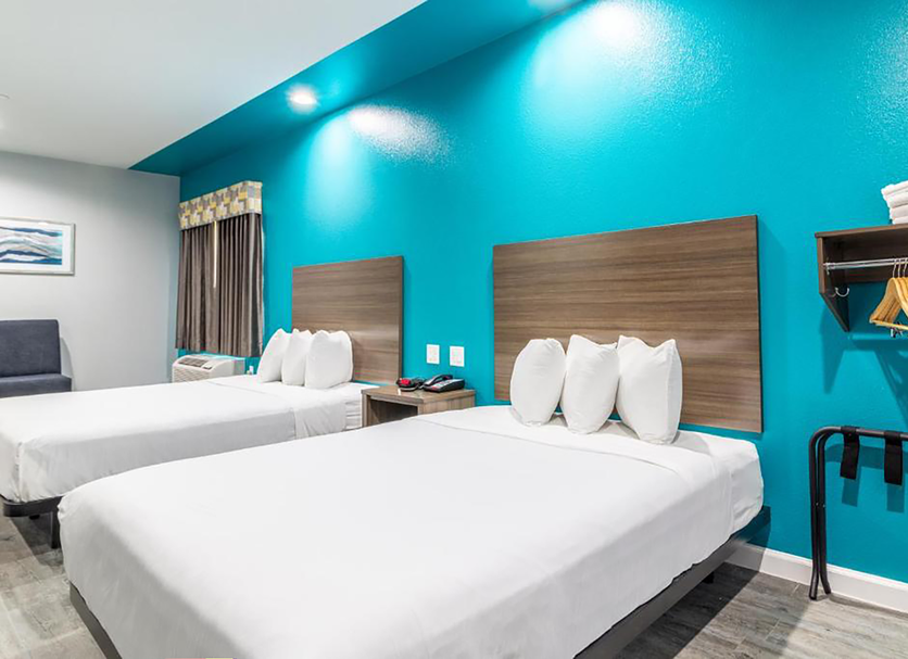 Scottish Inns & Suites - Kingwood in Humble with two white beds and a bright teal accent wall