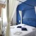 Hotel Noto Marina Vista Mare bedroom with blue feature wall, four-poster bed, and sheer curtains in Noto
