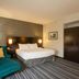 The Mosey Buffalo Williamsville, Tapestry Collection by Hilton guest room with king bed, chaise lounge, and wardrobe