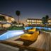 Niriides Beach in Kolympia with a lit outdoor pool, lounge chairs on a wooden deck, and palm trees at night