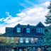Hotel Mountain Brook in Tannersville with peaked roof, large evergreen tree, and cloudy blue sky