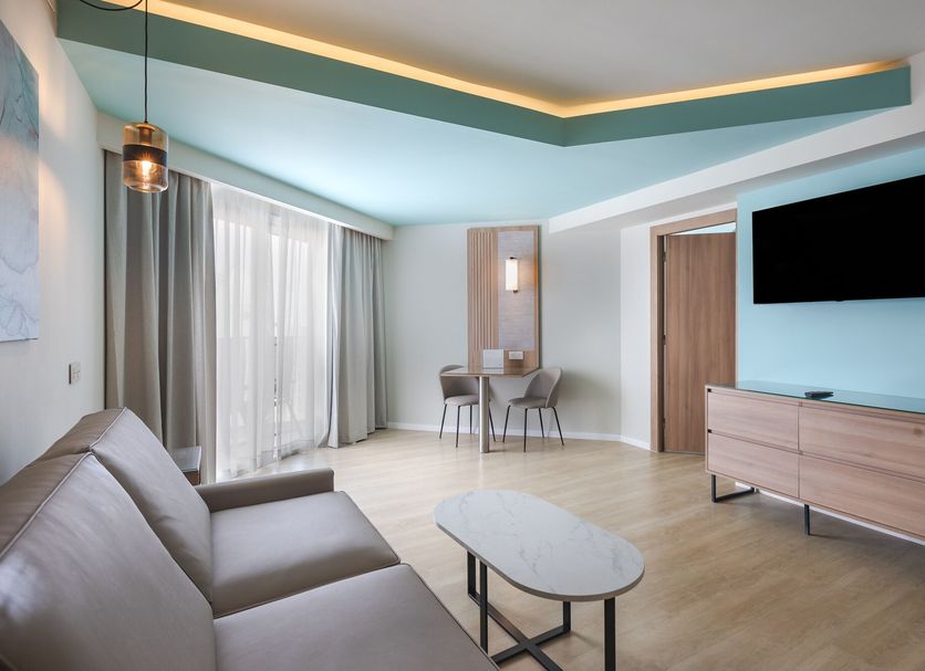 Riu Palace Antillas Adult Only in Noord, modern suite with sofa, TV, desk and balcony doors