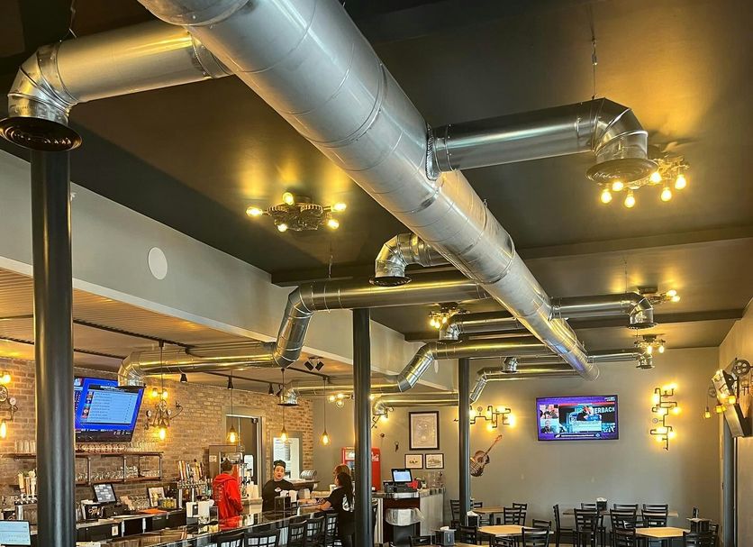 Hotel Whiskey in Pascagoula bar and dining area with tables, stools, exposed ductwork and TVs
