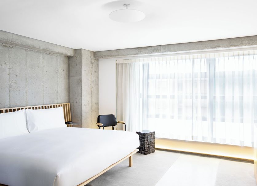 TUVE Hong Kong guest room with king bed, concrete walls, chair and large sheer-curtained window