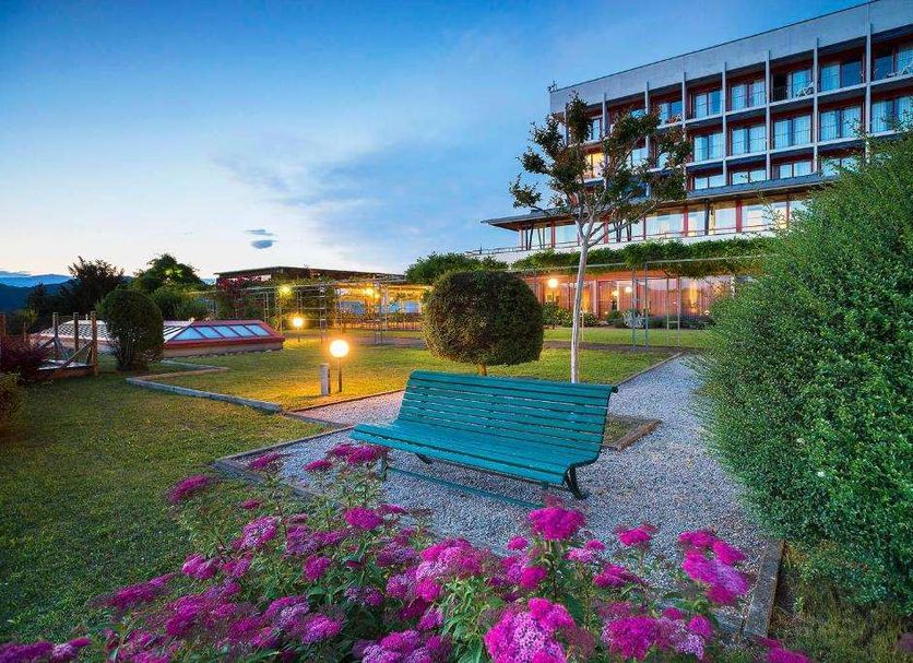 Hotel Serpiano in Brusino Arsizio with garden benches, flower beds and a modern lakeside building
