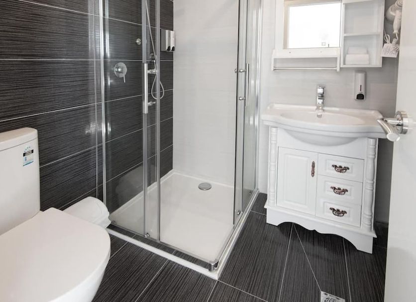 Lily Sands Inn bathroom in Melbourne with glass shower, white vanity, toilet and dark tiled floor