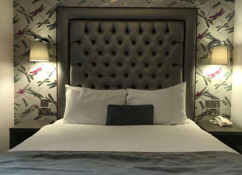 The Eaton Townhouse London guest room with tufted headboard, white bedding, bedside lamps and floral wallpaper
