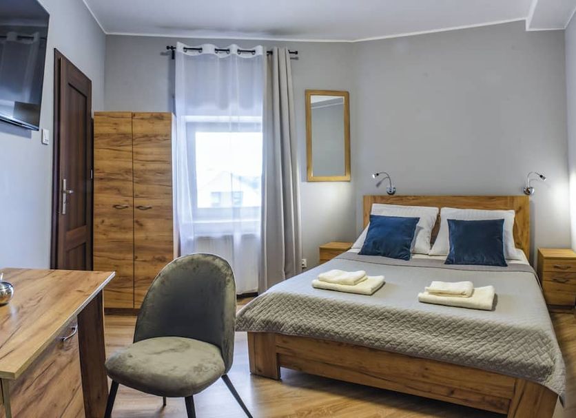Royal Gdansk guest room with wooden bed, wardrobe, desk, chair, and window in Gdansk