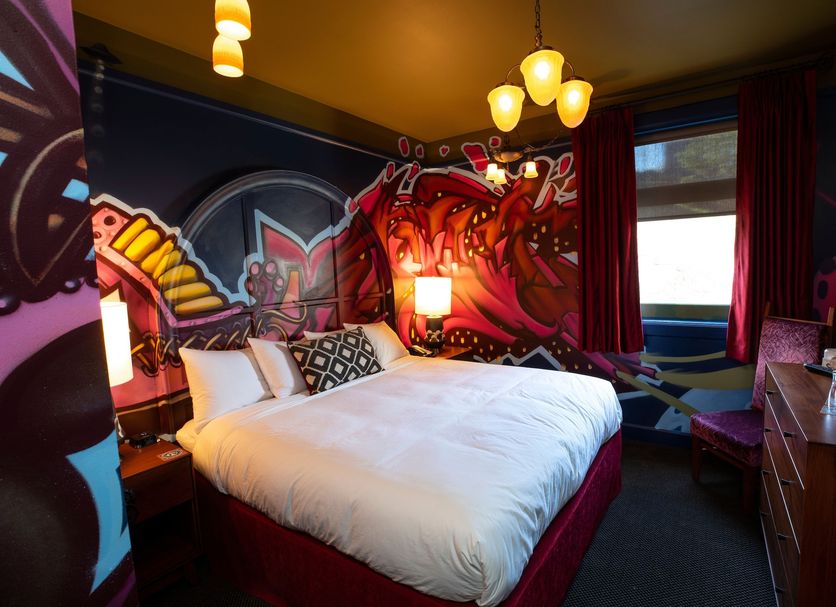 Mcmenamins Elks Temple Tacoma guest room with graffiti-style mural, white bed and hanging lights