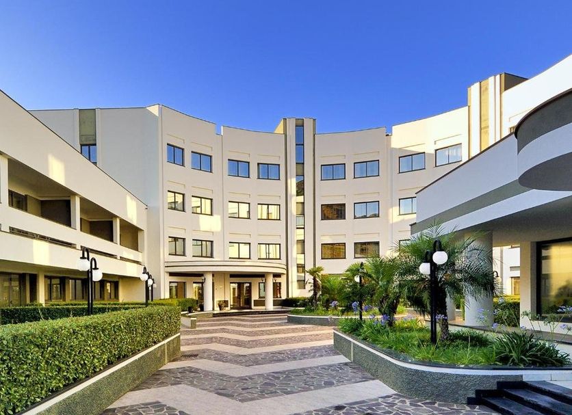 Park Hotel Mirabeau in Gasperina courtyard with landscaped paths and modern curved hotel facade
