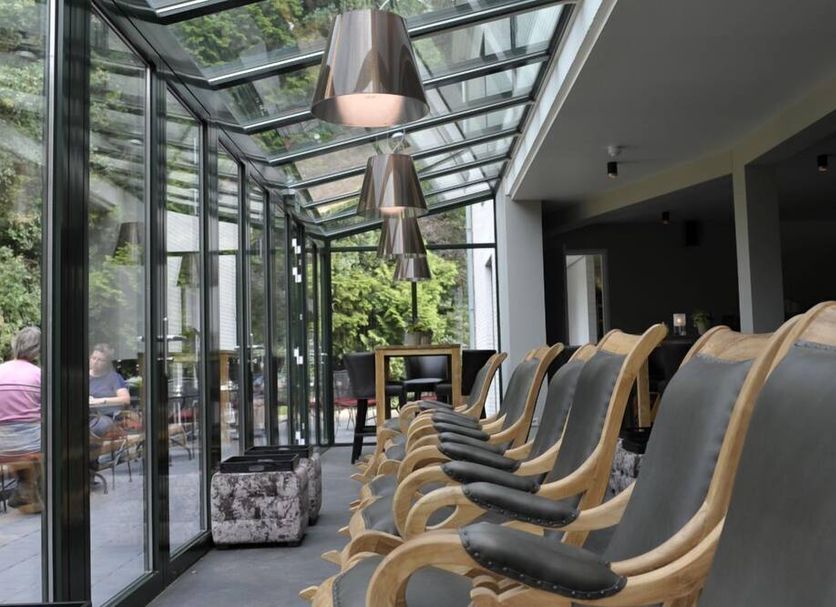 Glass-enclosed lounge at Landgoed Groot Warnsborn in Arnhem with rows of tan chairs and garden views
