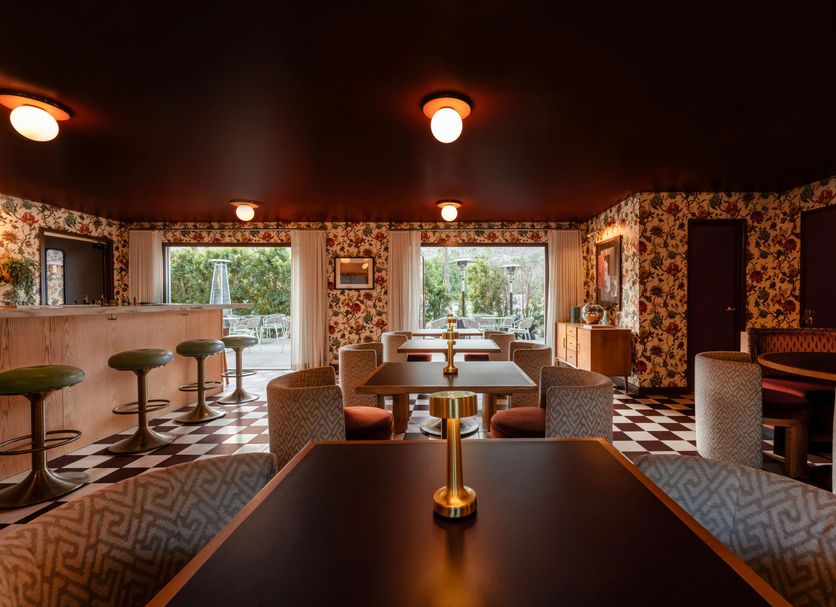 Royal Sun Palm Springs lounge with floral wallpaper, patterned seating, bar stools and large windows
