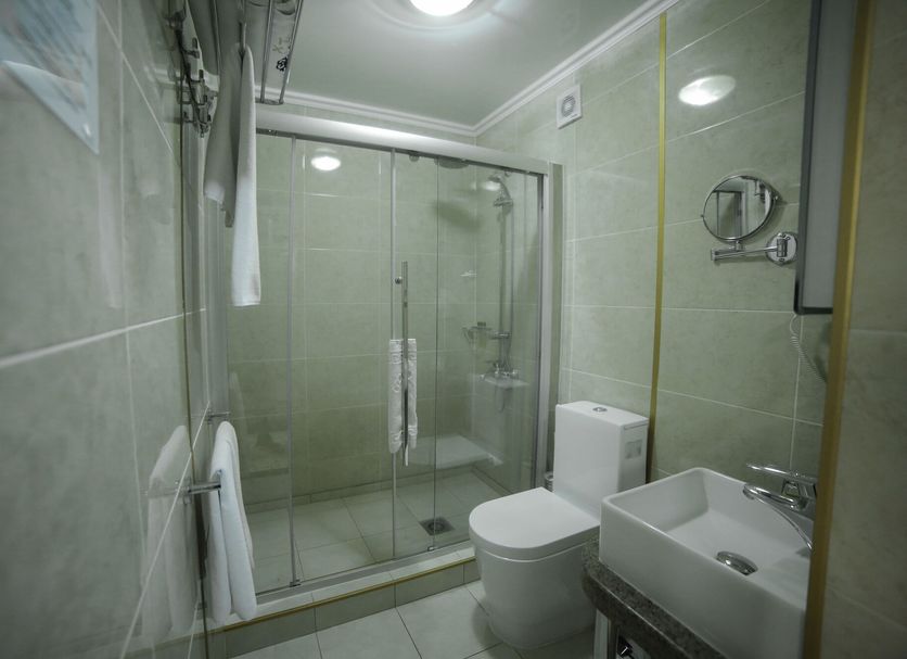 Onyx Hotel Bishkek bathroom with glass shower enclosure, toilet, and wall-mounted sink in Bishkek