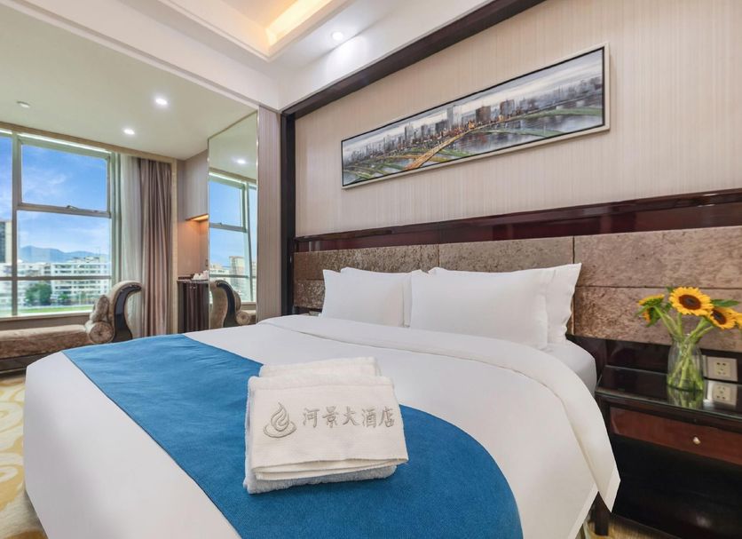 Riverview Hotel Guangzhou guest room with king bed, city view windows, and bedside sunflowers