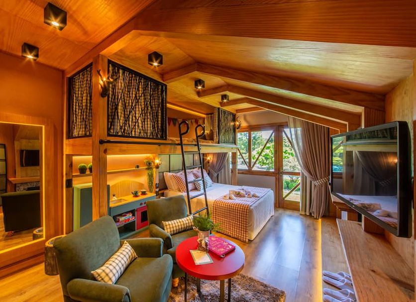 Hotel Alpestre in Gramado: cozy loft-style suite with wood سقiling, seating area, bed, and forest view