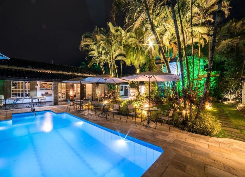 Casa Nostra Boutique Hotel in Paraty with a lit outdoor pool, palm trees, and patio seating at night
