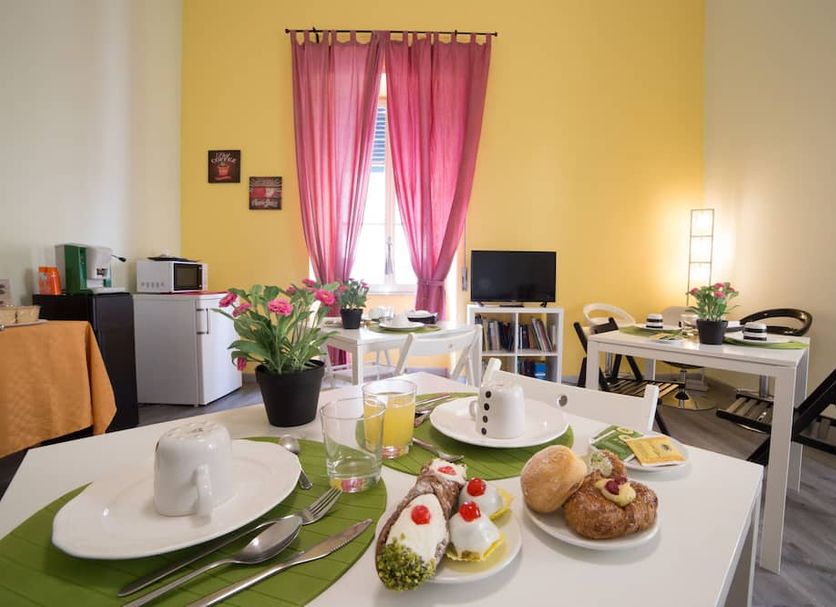 Tra L'Etna E Il Mare B&B in Catania: breakfast table with pastries, fruit, juice, and pink curtains