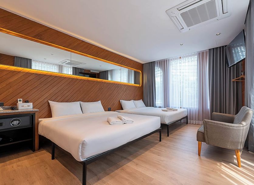 Boxpackers Pratunam Bangkok room with two beds, window curtains, armchair and wood-paneled accent wall