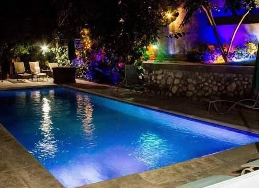 Elite Hotel Port Au Prince outdoor pool lit at night with lounge chairs and garden landscaping