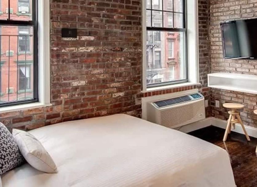 East Village Hotel New York room with exposed brick walls, large windows, bed, desk and wall-mounted TV
