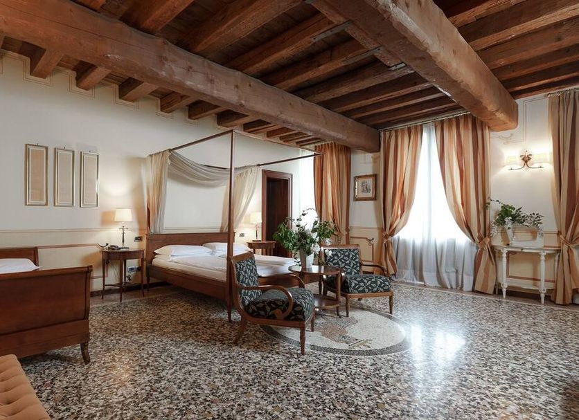 Hotel Villa Policreti in Aviano: airy guest room with exposed wood beams, four-poster bed and seating area