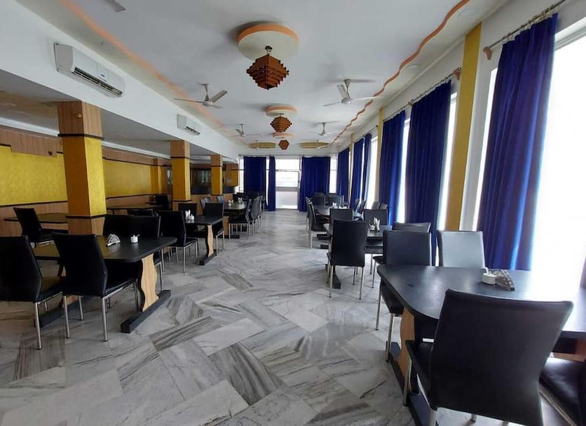 Hotel Sea Coast in Digha dining area with tables, chairs, marble floor, and large windows with blue curtains