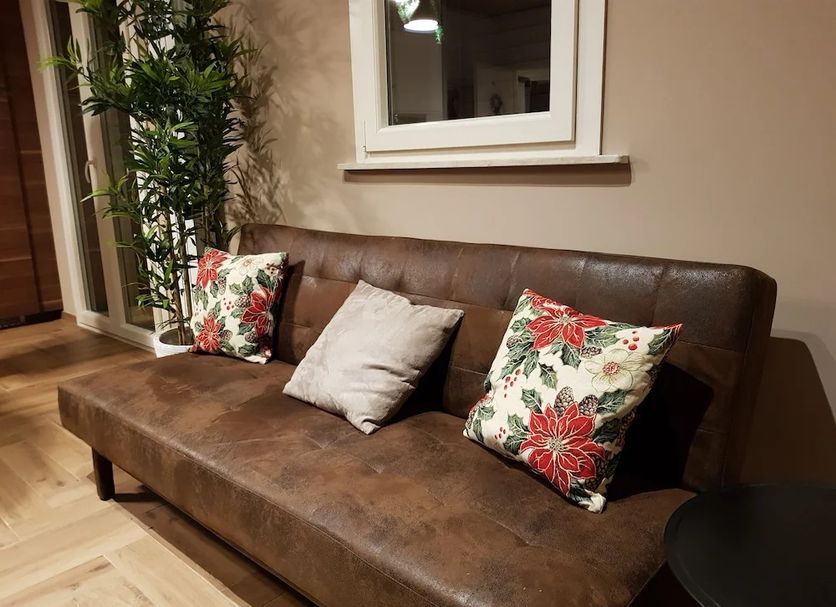Casa Vacanze Mgf Etna in Nicolosi: brown leather sofa with floral pillows beside a potted plant and window.