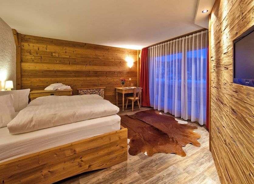 Arosa Vetter Hotel in Arosa guest room with wood-paneled walls, bed, TV and balcony curtains