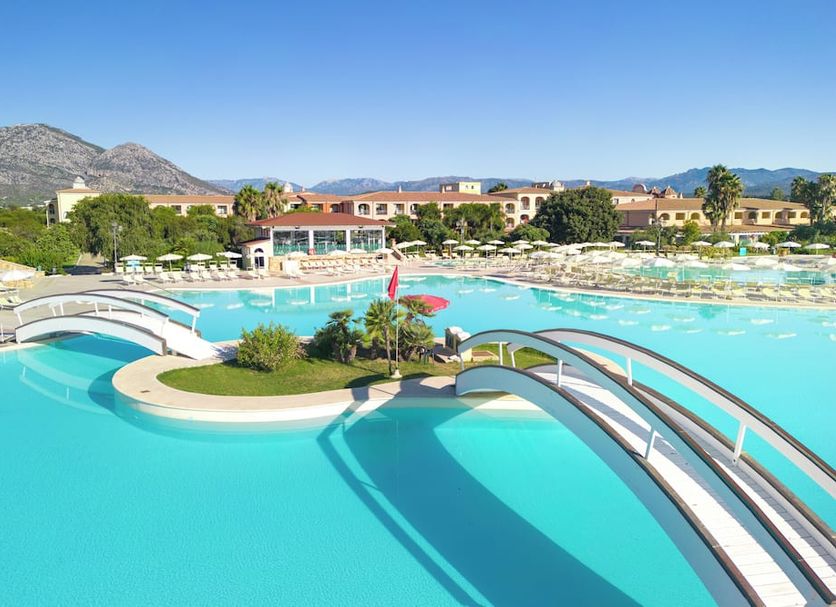 Club Hotel Marina Beach in Orosei: lagoon-style pool with arched bridges, palm island and mountain views
