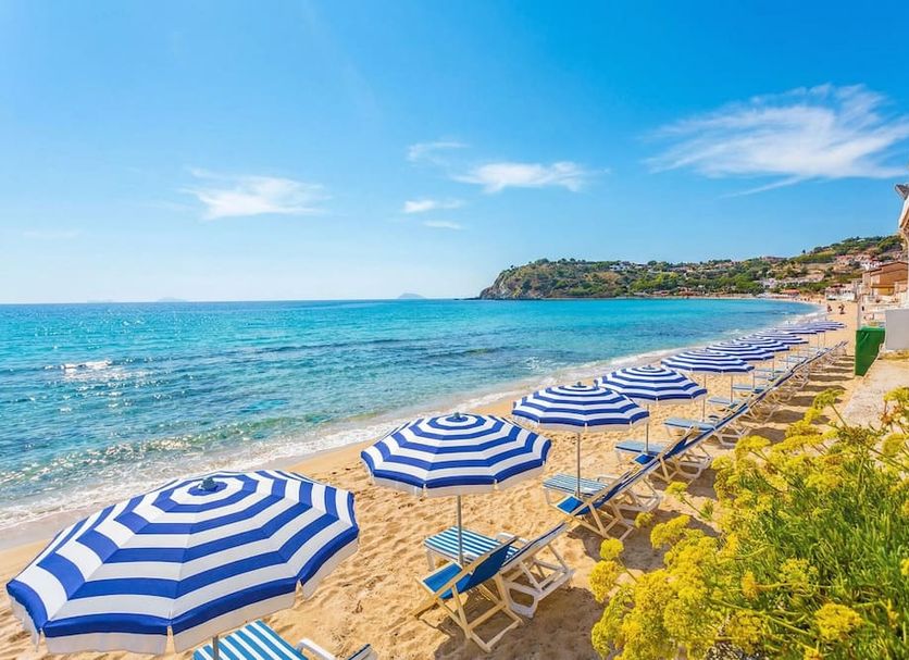 Hotel Ipomea Club in Ricadi with striped beach umbrellas and loungers on a sandy seaside beach