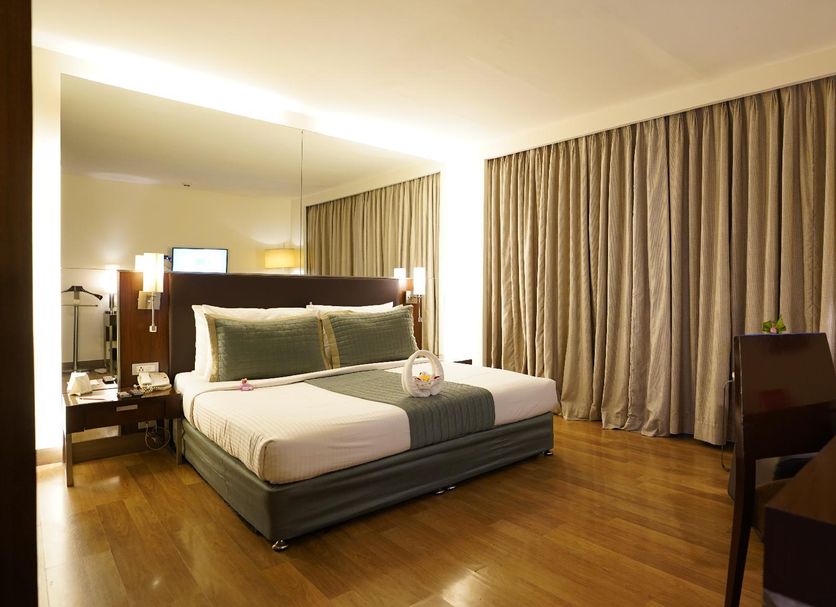 St Laurn Koregaon Park Pune guest room with king bed, wood floors, desk and floor-to-ceiling curtains