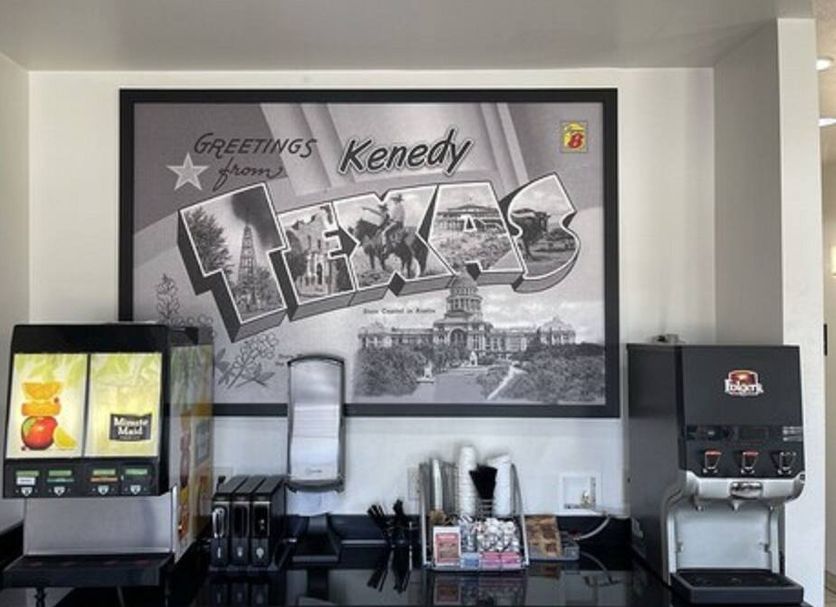 Breakfast area at Super 8 by Wyndham Kenedy with drink dispensers, coffee station and Texas wall art