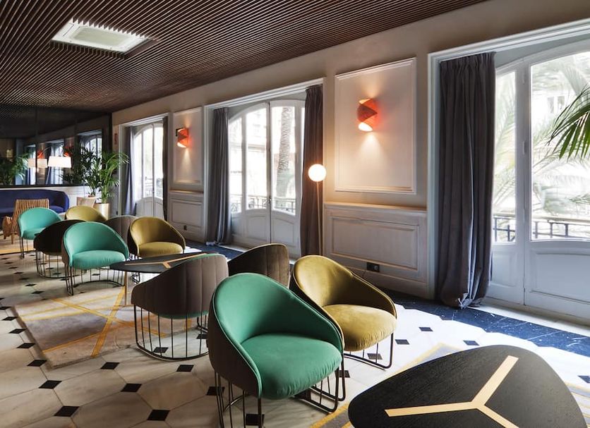 One Shot Reina Victoria in Valencia lobby seating area with chairs, tall windows, and patterned tile floor