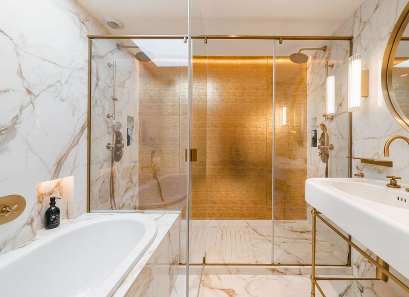 Hôtel Madison Paris bathroom with marble tub, glass shower, gold fixtures and round mirror