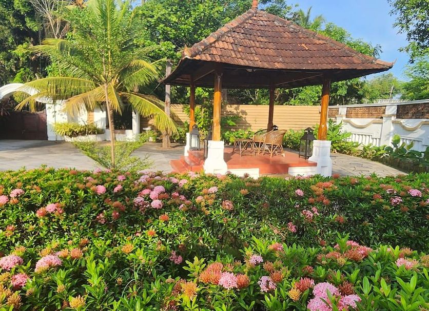 Tharavadu Heritage Home in Kumarakom: garden gazebo surrounded by pink flowers and palm trees