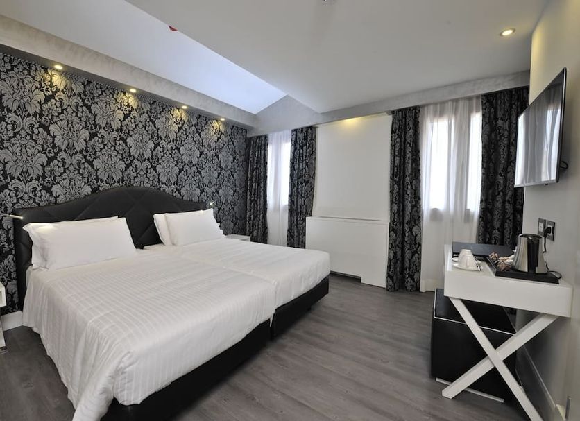 Al Theatro Palace in Venice guest room with king bed, patterned accent wall, and wall-mounted TV
