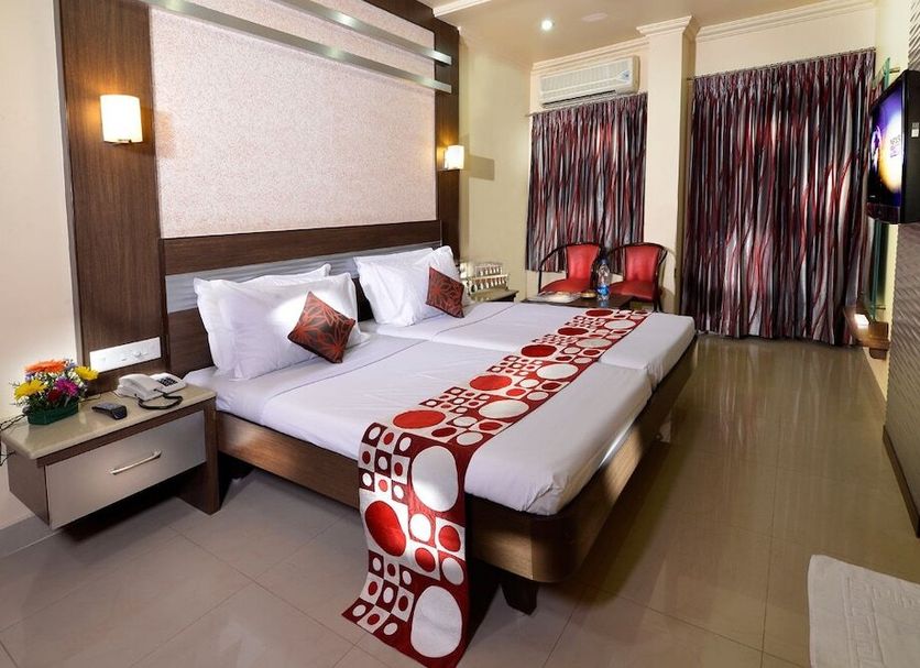 Hotel NavaRATNA Coimbatore guest room with king bed, bedside tables, curtains, and wall-mounted TV