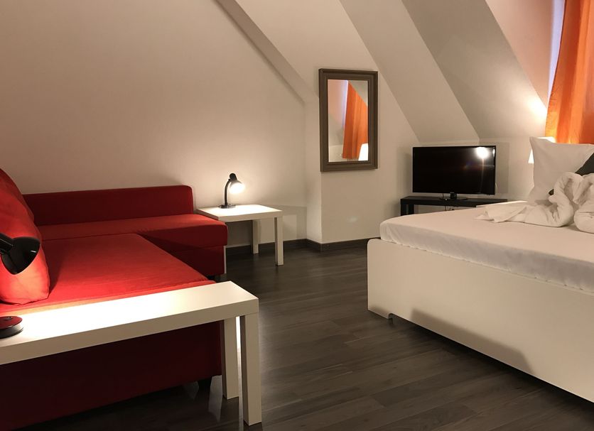 Inside Five Zurich attic room with red sofa, bed, TV and sloped ceiling