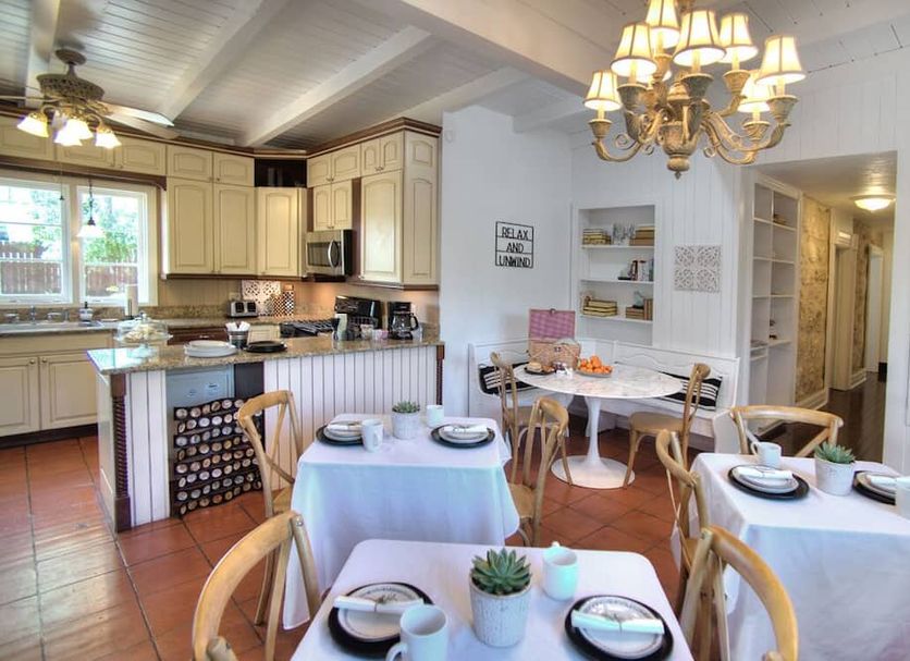The Evers House Fredericksburg dining room and kitchen with chandelier, tables set for breakfast, and kitchen island