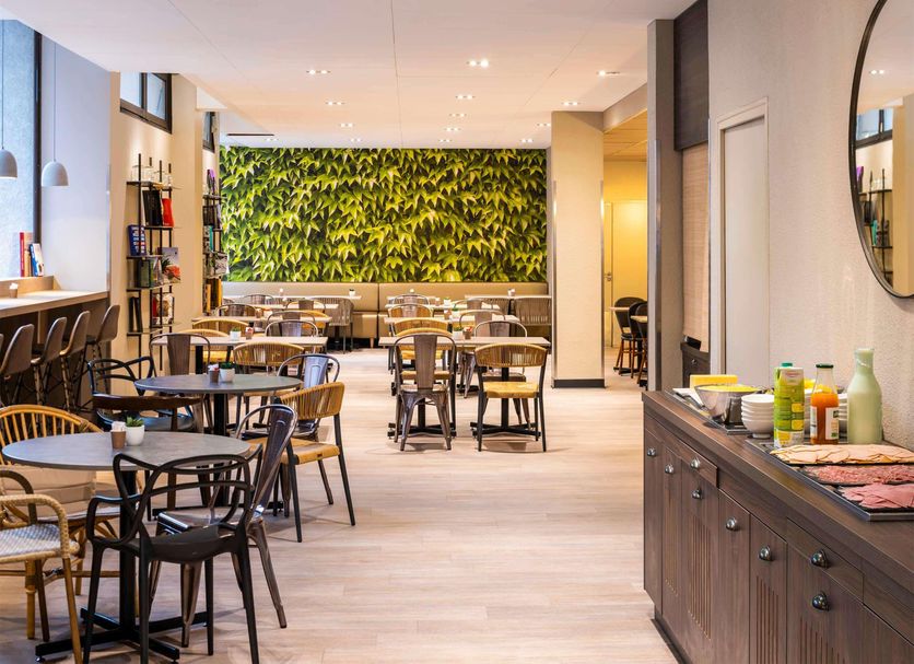 ibis Paris Alésia Montparnasse 14ème breakfast area in Paris with tables, chairs and a leafy wall
