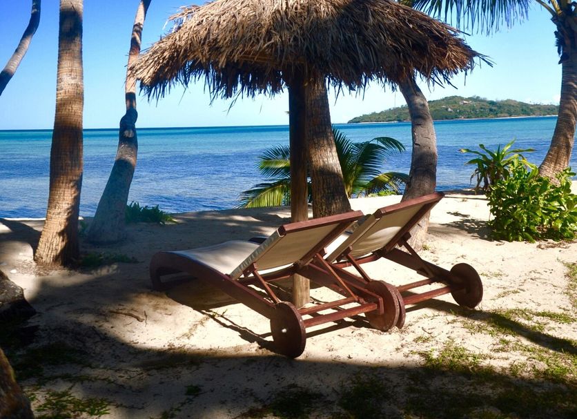 Coconut Beach Resort, Tavewa Island: beach loungers under a thatched umbrella by palm trees and the sea