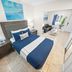 Beachside Gardens Apartments By Lowkl bedroom with blue bed, tile floor, sitting area and balcony in Deerfield Beach