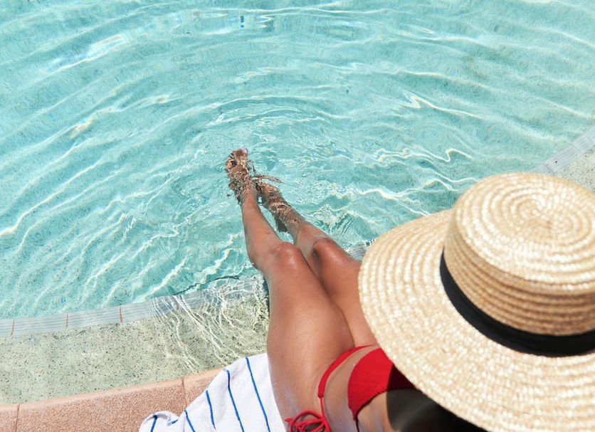 The Continental Hotel in Broome poolside scene with a guest relaxing by clear blue water and a sun hat