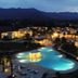 Spiagge San Pietro, Castiadas: illuminated resort pool and palm-lined grounds at dusk with mountain backdrop