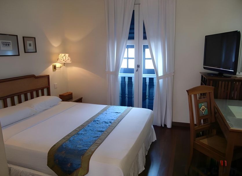 Perak Hotel Singapore guest room with bed, TV, desk and French doors to balcony