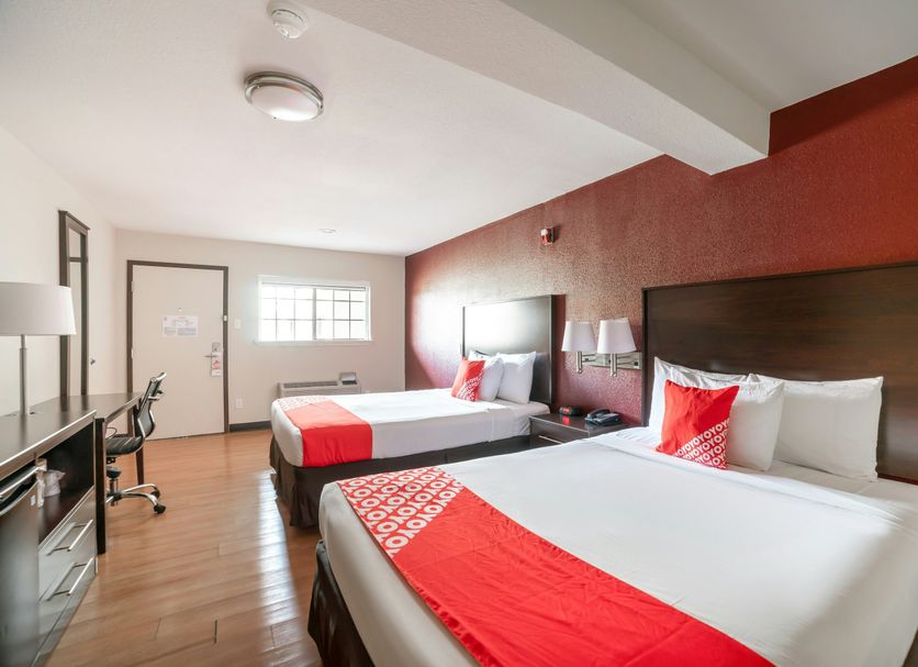OYO Hotel Mcallen Airport South guest room with two beds, red accent wall, desk and TV in McAllen