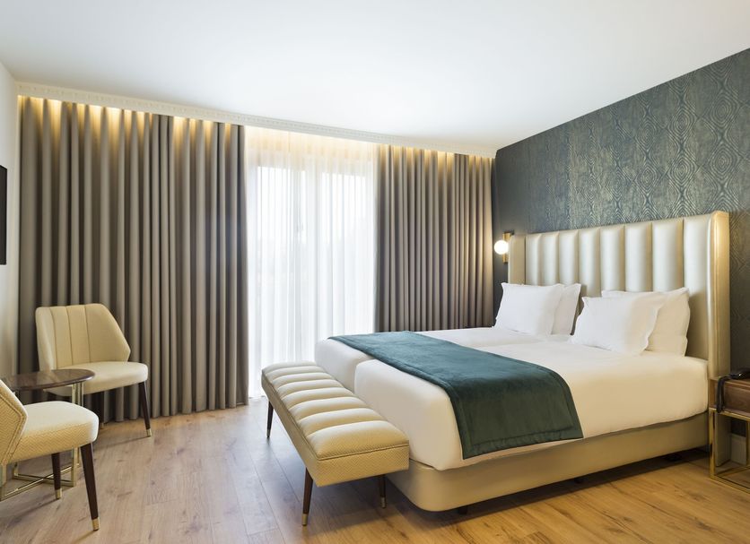 Acta The Avenue in Porto room with king bed, tufted headboard, bench, and floor-to-ceiling curtains