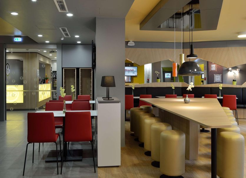 B&B Hotel Bonn-West in Bonn lobby lounge with red chairs, bar tables, and gold stools