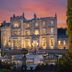 Crossbasket Castle in Glasgow, illuminated stone castle hotel with formal garden at sunset