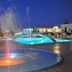 Hotel Lodos in Karterados: illuminated pool and fountain area at dusk with arched building backdrop